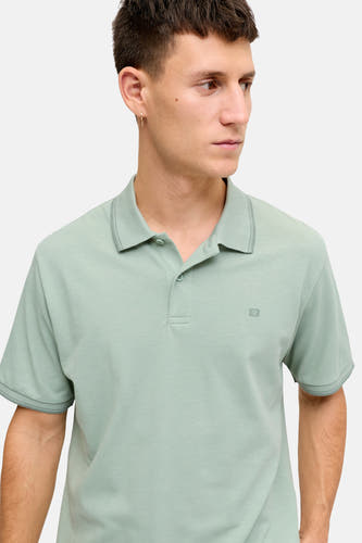 Polo verte JJREBEL de couleur verte avec structure piquée, coutures plus foncées sur le col et les poignets, et un logo 'R'.