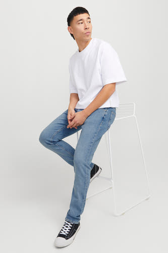 Lichtblauwe slim fit jeans van Jack & Jones Jeans Intelligence, gedragen met een wit T-shirt en zwarte sneakers op een witte stoel.
