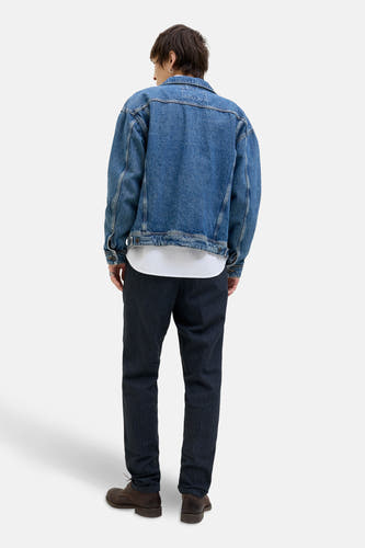 Jean chino bleu de JACK & JONES JEANS INTELLIGENCE, associé à une veste en cuir, un T-shirt blanc et des chaussures marrons.