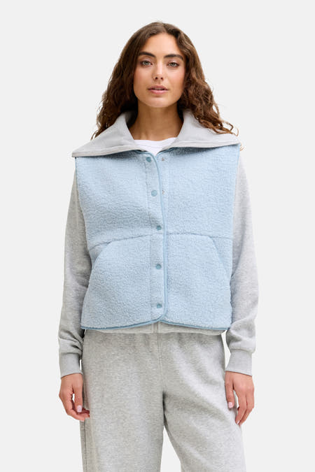 Gilet bodywarmer bleu de JJXX, avec fermeture à boutons et texture polaire, porté sur un pull gris et un pantalon de jogging.
