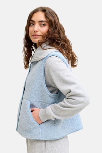 Gilet de corps bleu JJXX, avec texture en fourrure, porté sur un pull gris et un pantalon de jogging.