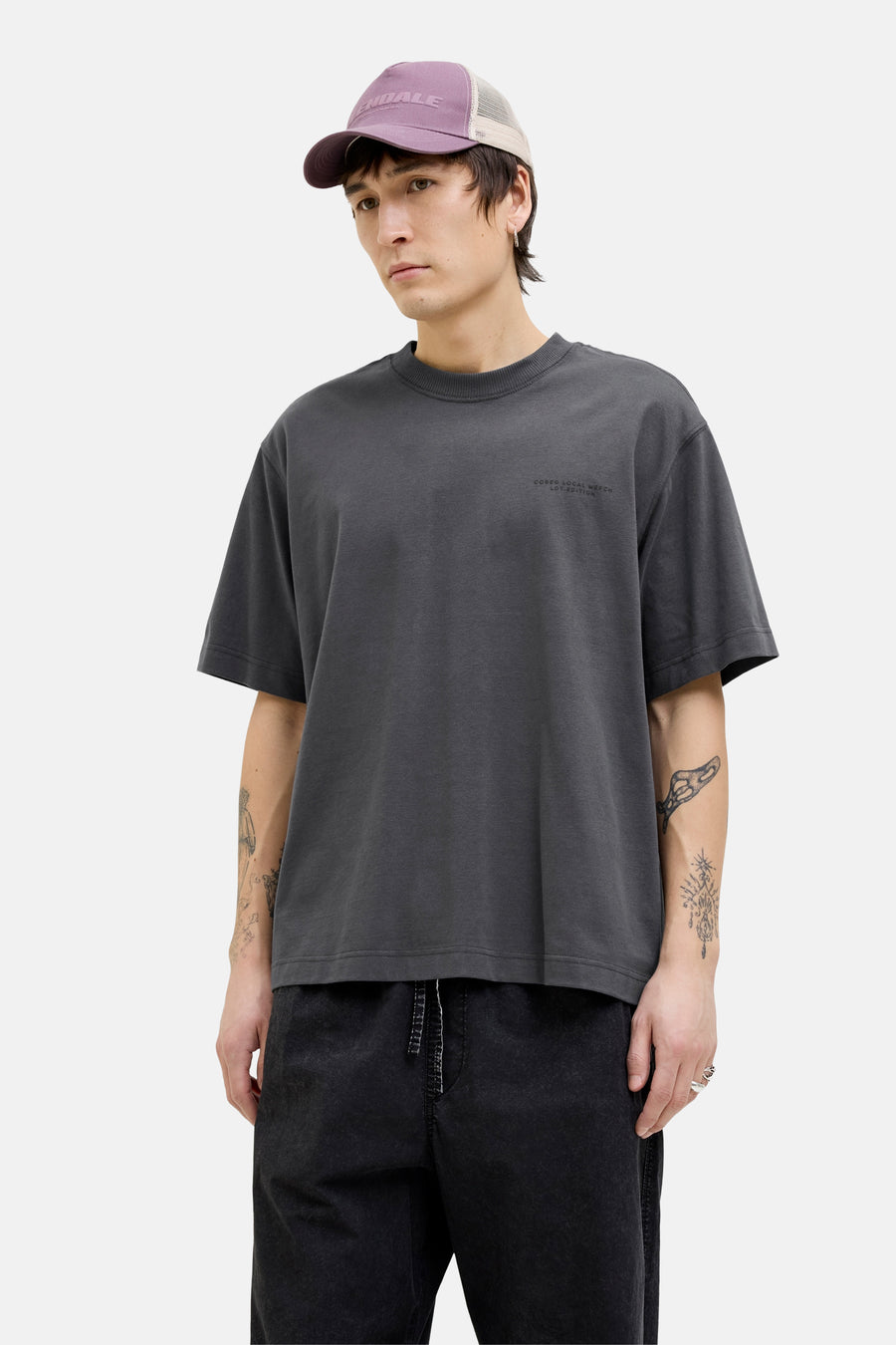 T-shirt gris à manches courtes de CORE BY JACK & JONES, avec texte sur la poitrine, porté avec une casquette et un pantalon noir.