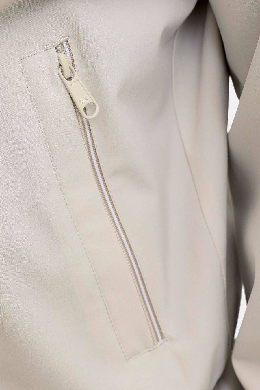 Manteau court beige de PREMIUM by JACK & JONES avec une fermeture éclair partiellement ouverte à motif rayé et un détail de logo sur la fermeture éclair.
