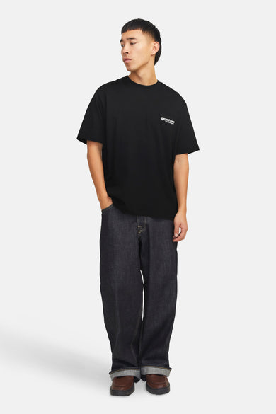T-shirt noir à manches courtes de CORE BY JACK & JONES, porté avec des jeans larges et des chaussures marrons.