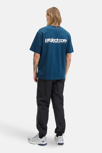 T-shirt bleu à manches courtes de CORE BY JACK & JONES, dos visible, associé à un short d'entraînement noir avec une bande blanche et des baskets grises.