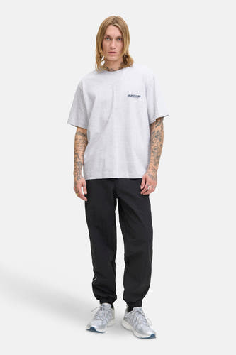 T-shirt gris à manches courtes de CORE BY JACK & JONES, avec un petit logo sur la poitrine, porté avec un pantalon noir et des baskets.