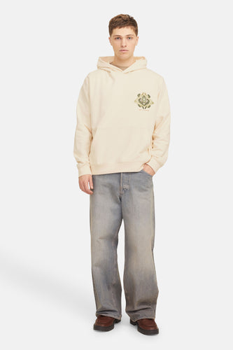 Man in beige hoodie, wijde jeans, bruine schoenen.