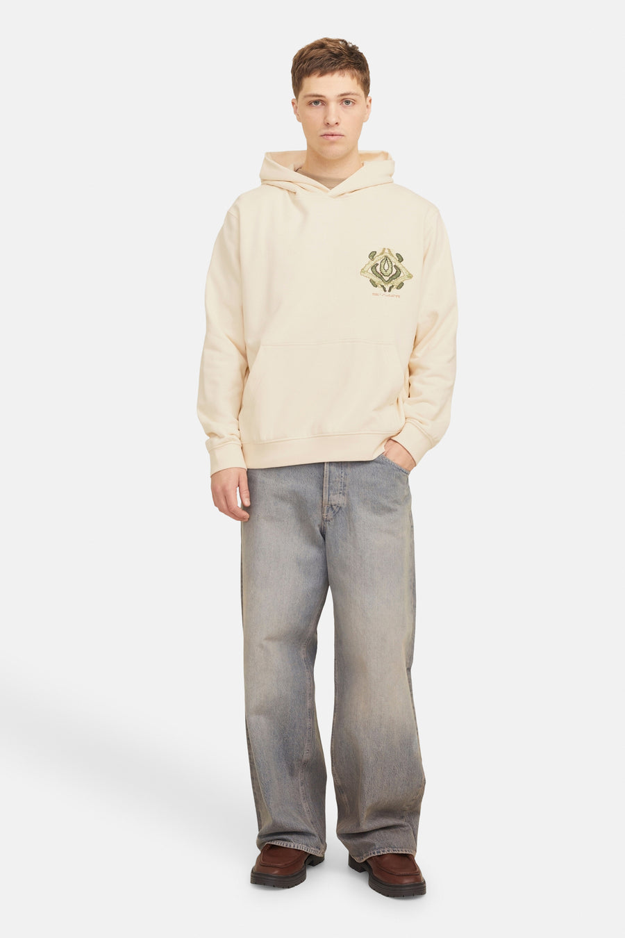 Man in beige hoodie, wijde jeans, bruine schoenen.