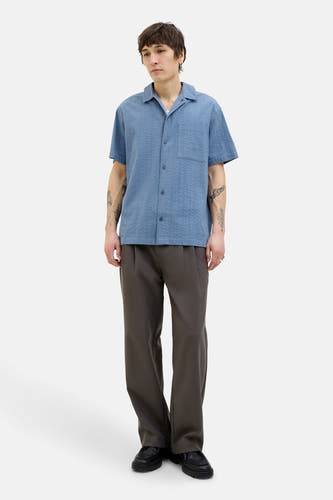Chemise bleue à manches courtes de PREMIUM BLUE par JACK & JONES, avec un motif texturé subtil, portée avec un pantalon gris et des chaussures noires.