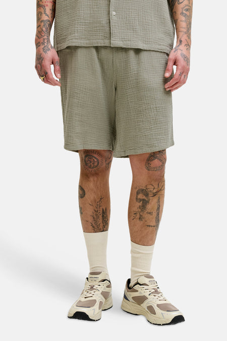 Short vert de ORIGINALS BY JACK & JONES, avec une texture froissée, porté avec des chaussettes de couleur crème et des baskets de style rétro.