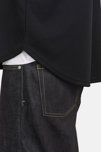 Zwarte trui, donkere jeans met stiksels, witte t-shirt zichtbaar.