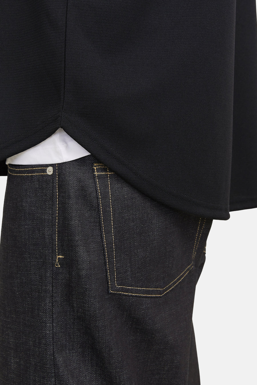 Zwarte trui, donkere jeans met stiksels, witte t-shirt zichtbaar.