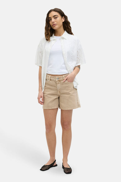 Short beige de JJXX, associé à un T-shirt blanc et un chemisier blanc ouvert avec des détails en bordure.