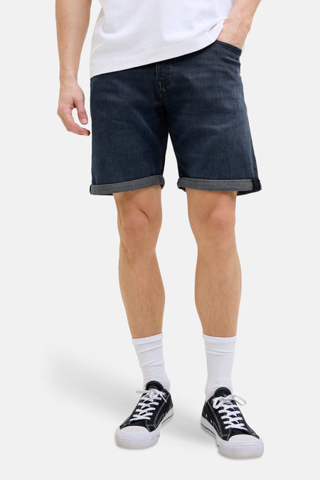 Short en jean bleu foncé de JACK & JONES JEANS INTELLIGENCE, avec ourlets retroussés, porté avec un t-shirt blanc, des chaussettes et des baskets.