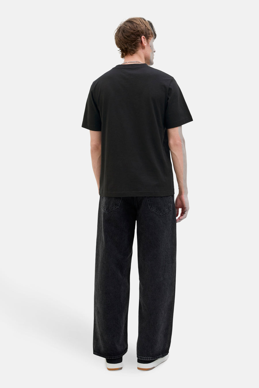 Zwart T-shirt met korte mouwen van CORE BY JACK & JONES, gezien van achteren, met wijde, donkere jeans en witte schoenen.