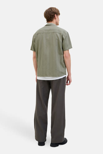 Chemise verte à manches courtes de PREMIUM BLUE par JACK & JONES, avec un motif subtil de fines lignes verticales, portée avec une chemise blanche et un pantalon gris.