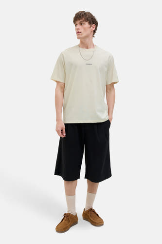 T-shirt écru à manches courtes d'ORIGINALS BY JACK & JONES, associé à une chaîne argentée, porté avec des short noirs larges et des chaussures marrons.