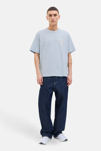 T-shirt bleu à manches courtes d'ORIGINALS BY JACK & JONES, avec un petit imprimé graphique et porté avec des jeans foncés et des baskets blanches.