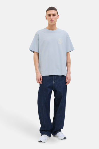 T-shirt bleu à manches courtes d'ORIGINALS BY JACK & JONES, avec un petit imprimé graphique et porté avec des jeans foncés et des baskets blanches.