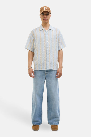 Chemise bleue claire à manches courtes d'ORIGINALS BY JACK & JONES, avec des rayures verticales et portée avec un chapeau, des jeans et des chaussures en cuir de mouton.