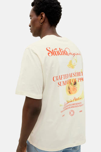 T-shirt écru à manches courtes d'ORIGINALS BY JACK & JONES, avec une impression vintage sur le dos et porté avec un jean.