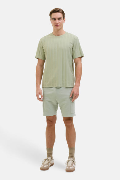 T-shirt vert avec manches courtes de JJREBEL, doté d'un motif de fines rayures verticales et porté avec des shorts et des baskets.