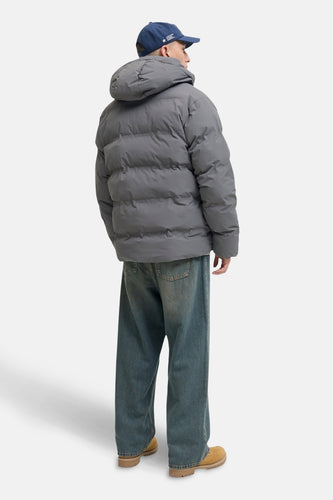 Achterkant van een man in een grijze pufferjas, wijde jeans en bruine schoenen.