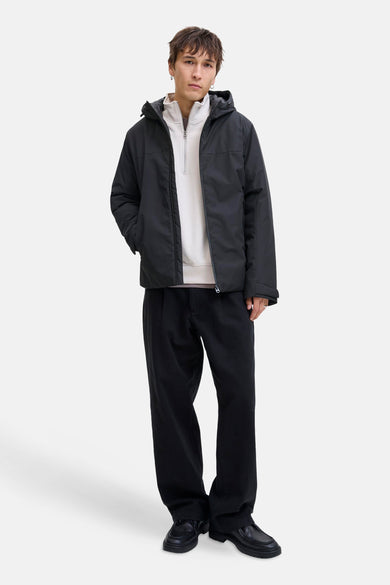 Manteau court noir de CORE BY JACK & JONES, avec capuche et porté avec un pull blanc et un pantalon noir.
