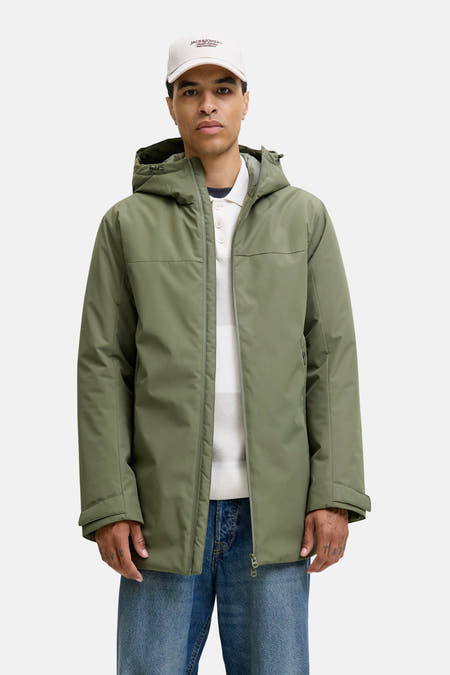 Manteau court vert de ORIGINALS BY JACK & JONES, avec capuche, porté sur une chemise rayée et des jeans bleus.