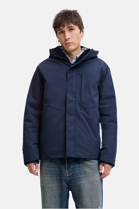 Manteau court bleu de CORE BY JACK & JONES, avec capuche, porté sur un chemisier rayé et un jeans bleu.
