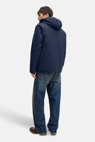 Blauwe korte jas van CORE BY JACK & JONES, met capuchon en gecombineerd met wijde jeans en bruine schoenen.
