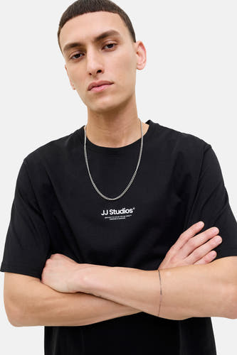 T-shirt noir à manches courtes de CORE BY JACK & JONES, avec une chaîne argentée et des bras croisés.