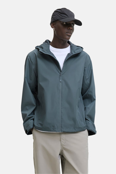 Manteau court gris d'ORIGINALS BY JACK & JONES, avec capuchon et un T-shirt blanc et une pantalon beige.