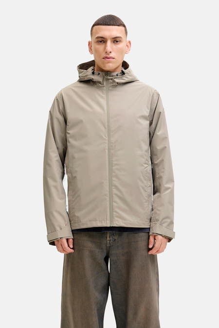 Manteau court beige d'ORIGINALS BY JACK & JONES, avec un capuchon, porté sur un pull bordeaux à l'logo Harvard.