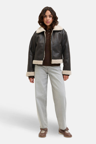 Manteau court brun de JJXX avec doublure crème, associé à un pull brun et des jeans gris.