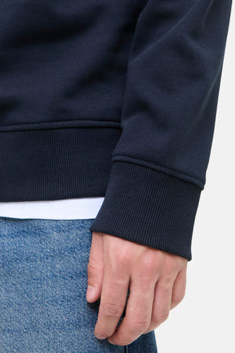Pull-over bleu d'ORIGINALS BY JACK & JONES, à manches longues et bordures côtelées, porté avec un pantalon de travail.