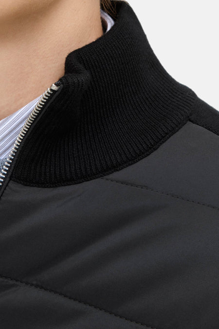 Zwart gewatteerd vest met gebreide kraag en zilveren rits.

