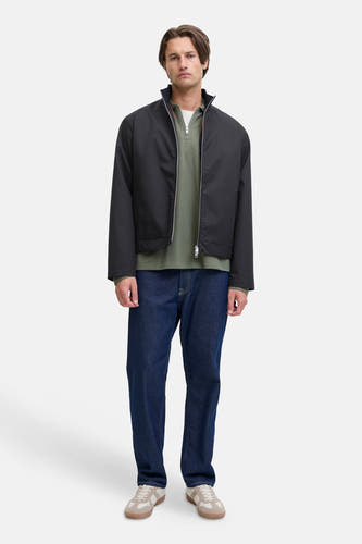 Manteau court noir de JJREBEL, porté avec un t-shirt vert à manches longues et des jeans bleu marine et des baskets crème.