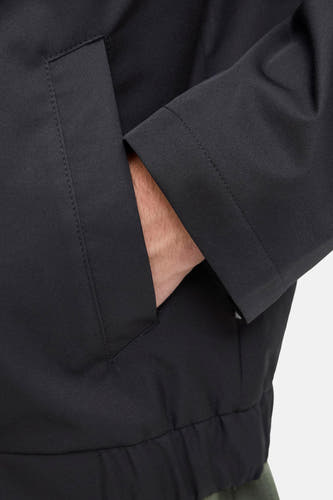 Manteau court noir de JJREBEL, avec les mains dans les poches et une bande élastique en bas.