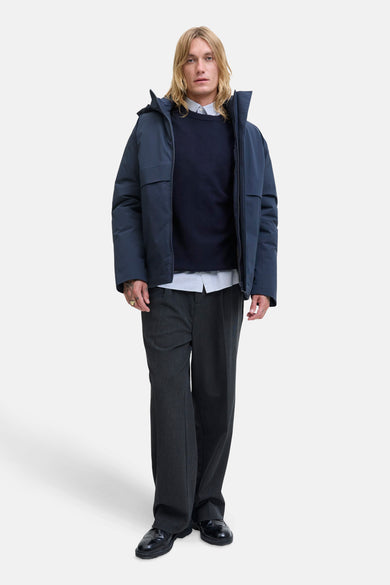 T-shirt bleu avec col rond de PREMIUM par JACK & JONES, porté sur un chemisier rayé, avec un pantalon gris et des chaussures noires.
