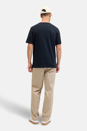 Achterkant van een man in een donkerblauw T-shirt, beige broek en beige pet.