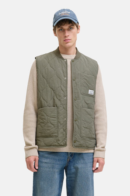 Gilet vert de ORIGINALS BY JACK & JONES, avec une broderie en forme de lunettes, porté sur un gilet beige et des jeans bleus.