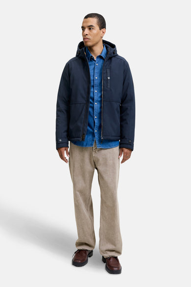 Manteau bleu court de PREMIUM BLUE par JACK & JONES, porté avec un chemisier en denim et un pantalon beige.