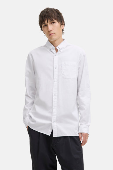 Chemise blanche à manches longues de PREMIUM by JACK & JONES, avec une poche po poitrine et portée avec un pantalon noir.
