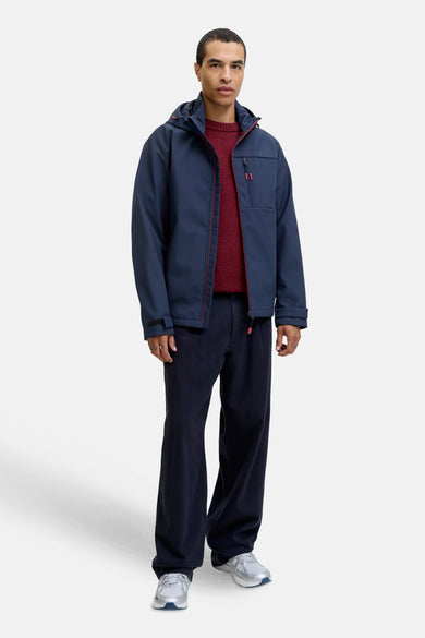Veste courte bleue de CORE BY JACK & JONES, avec des détails rouges et portée avec un pull rouge et un pantalon foncé.