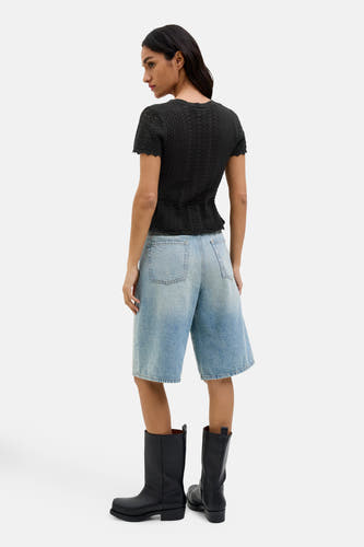 Pull-over noir de JJXX, avec des manches courtes et un subtil motif ajouré, porté avec des bermudas en denim bleu et des bottes noires.