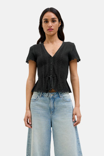 Pull noir JJXX, à manches courtes, avec une fermeture à boutons et une ceinture élastique, associé à un pantalon de denim large.