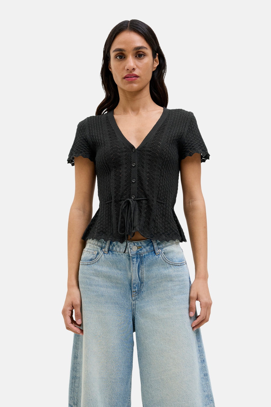 Pull noir JJXX, à manches courtes, avec une fermeture à boutons et une ceinture élastique, associé à un pantalon de denim large.