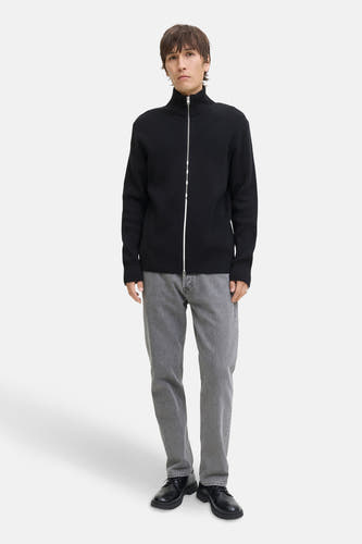 Gilet noir de CORE BY JACK & JONES, avec une fermeture éclair argentée, associé à des jeans gris et des chaussures noires.