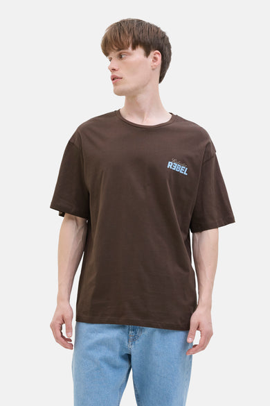 T-shirt marron à manches courtes de JJREBEL, avec une impression bleu clair en haut à droite, porté avec un jeans bleu.